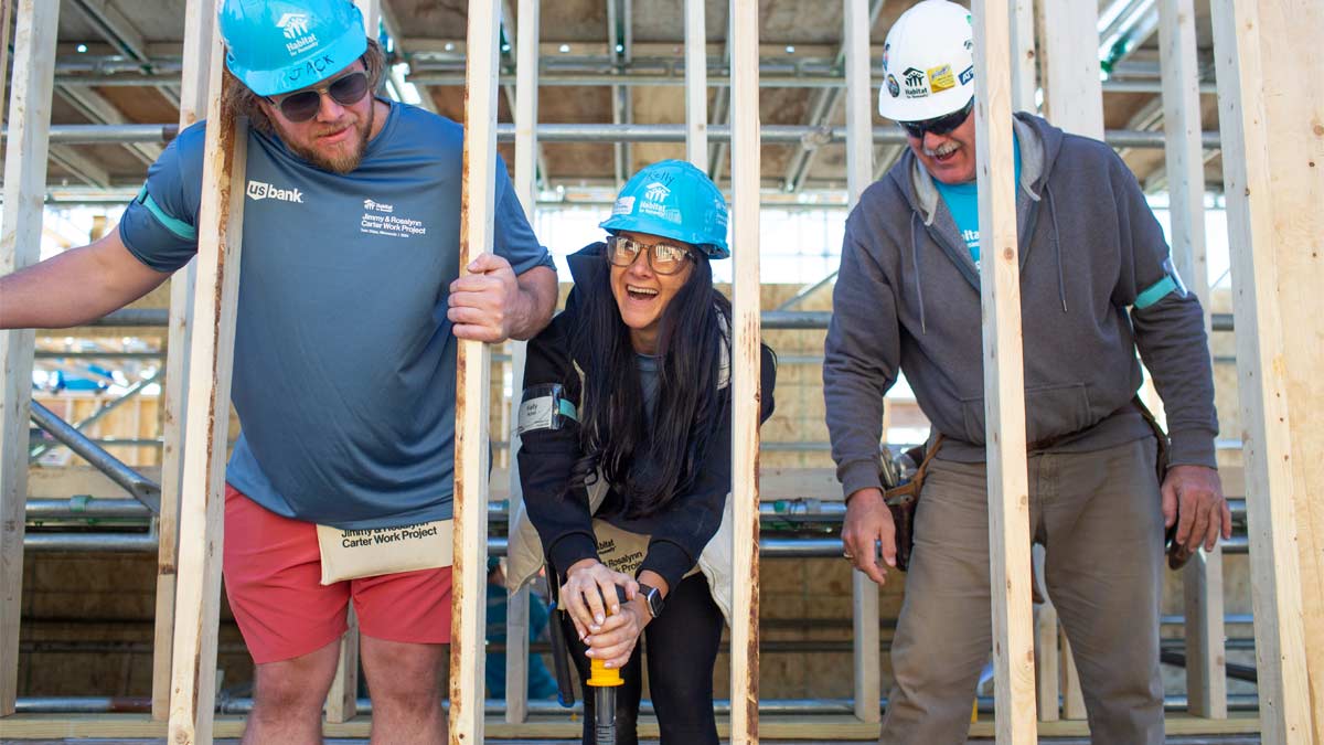 Photo of three people in hard hats constructing a house.