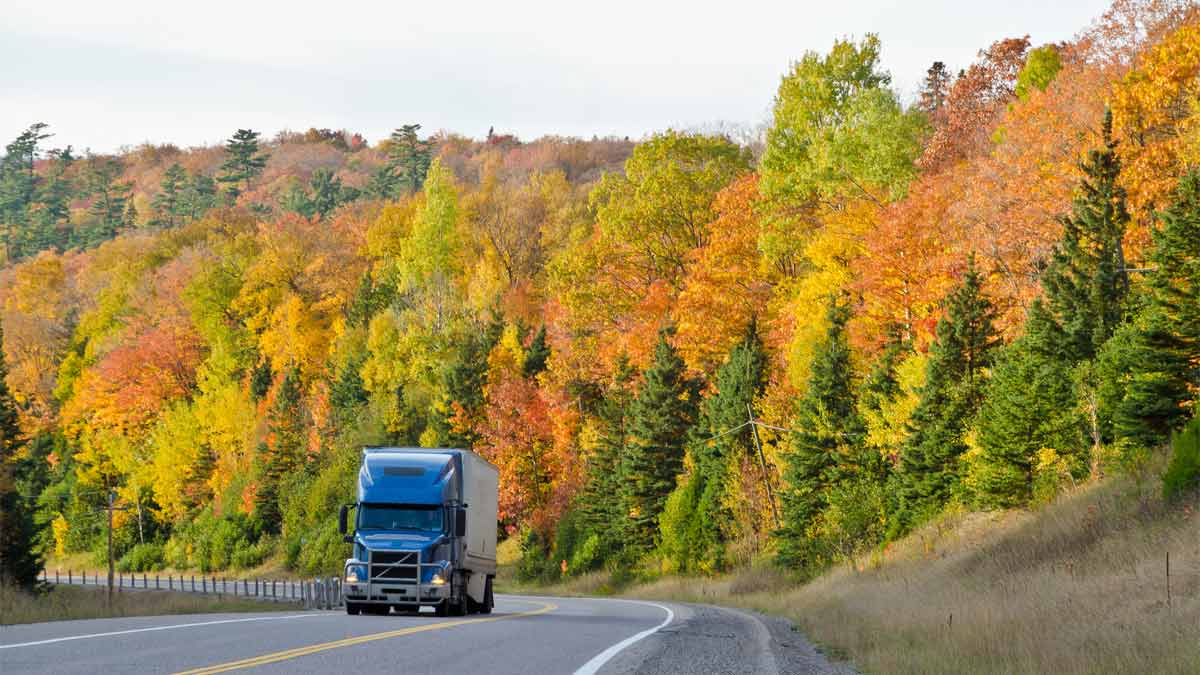 Photo of semi truck driving on highway alongside autumn color