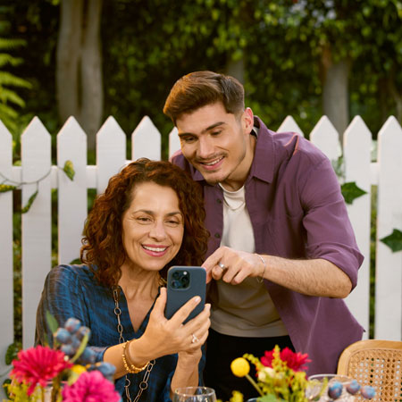 A son is showing his mom something on her phone while they’re outdoors in a garden.