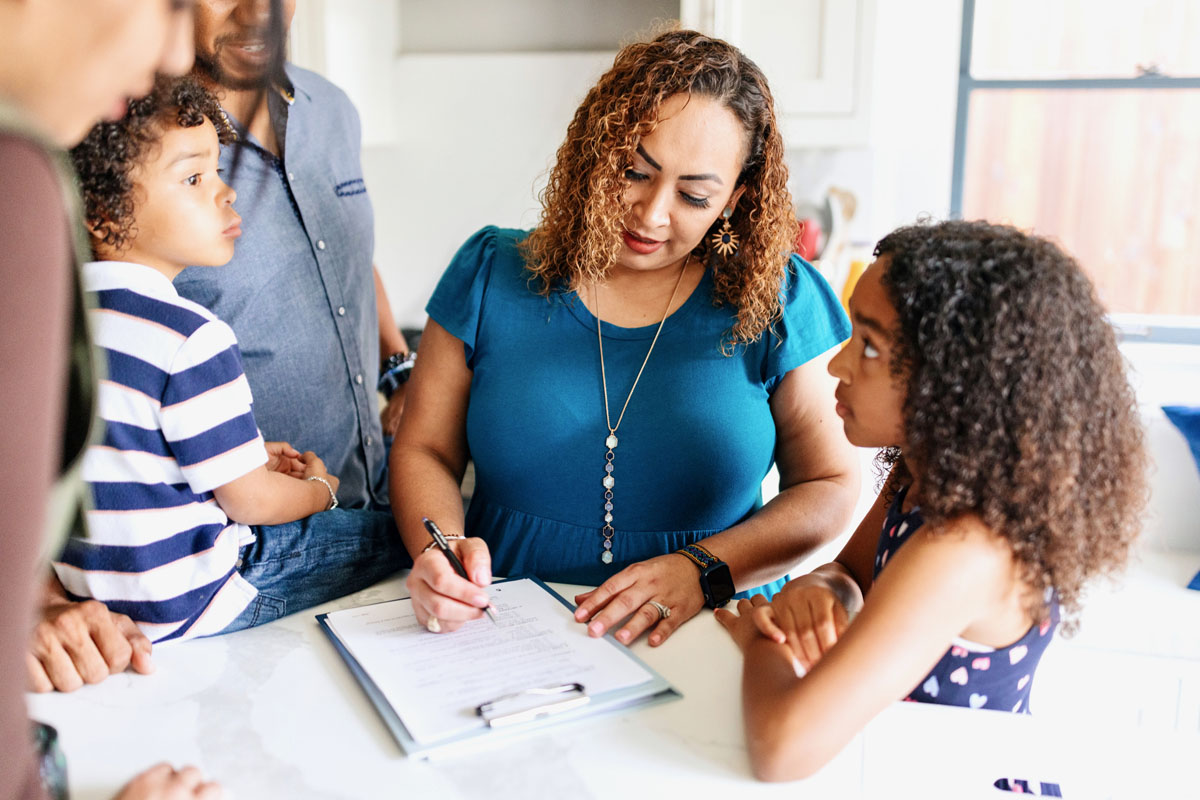 woman signing paperwork with her kids nearby