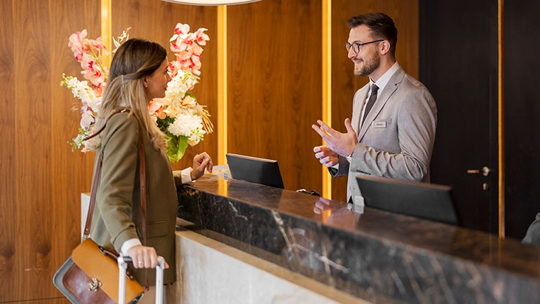 Woman business traveler checking into a hotel and speaking to a man at the front desk.