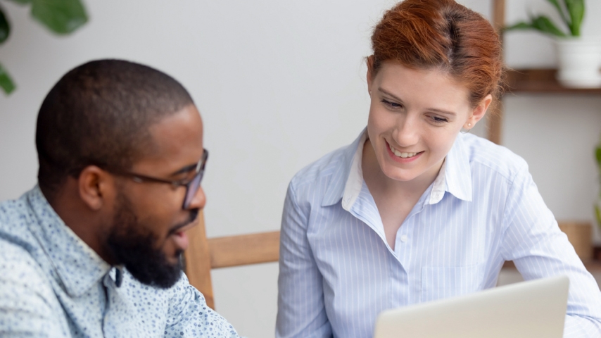 Two people looking at a laptop with one person pointing at the laptop screen.