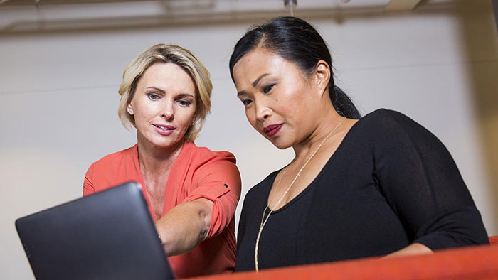 Two women standing next to each other and looking at a laptop.