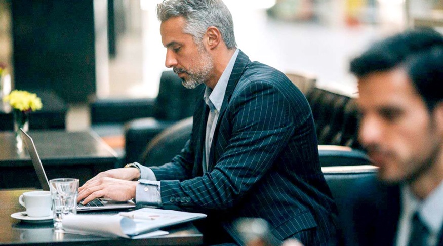 Man at desk with laptop comparing bank and boutique alternative fund and asset management services.