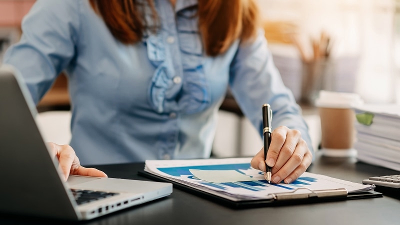 Woman writing on a clipboard with one hand and typing on a laptop with the other