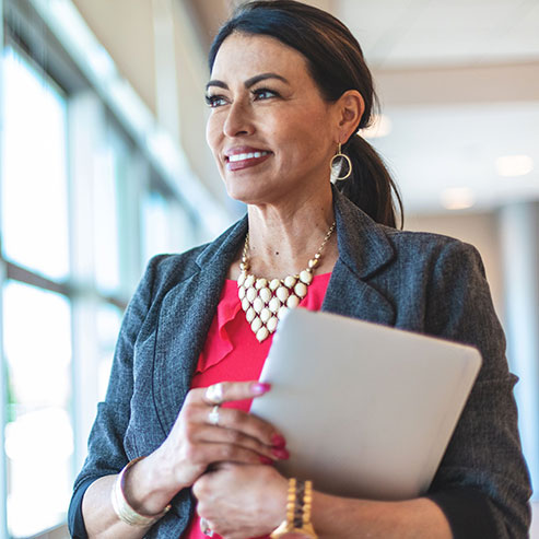 Professional woman standing in front of window and holding a tablet device.