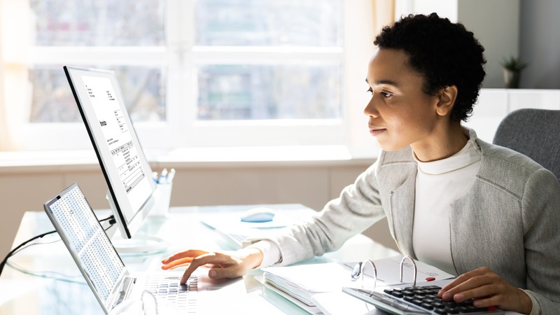 Professional woman at a desk looking at charts on a computer monitor.