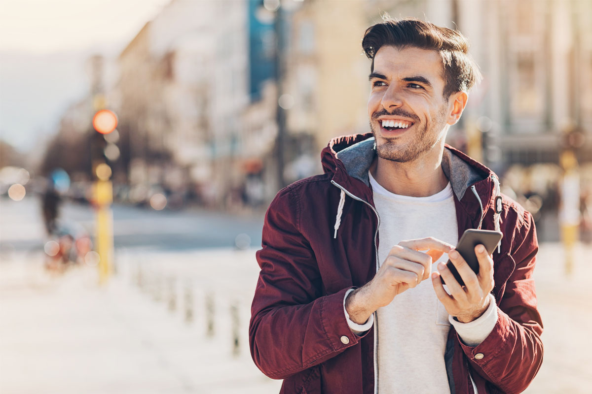 Man smiling and using smartphone outdoors