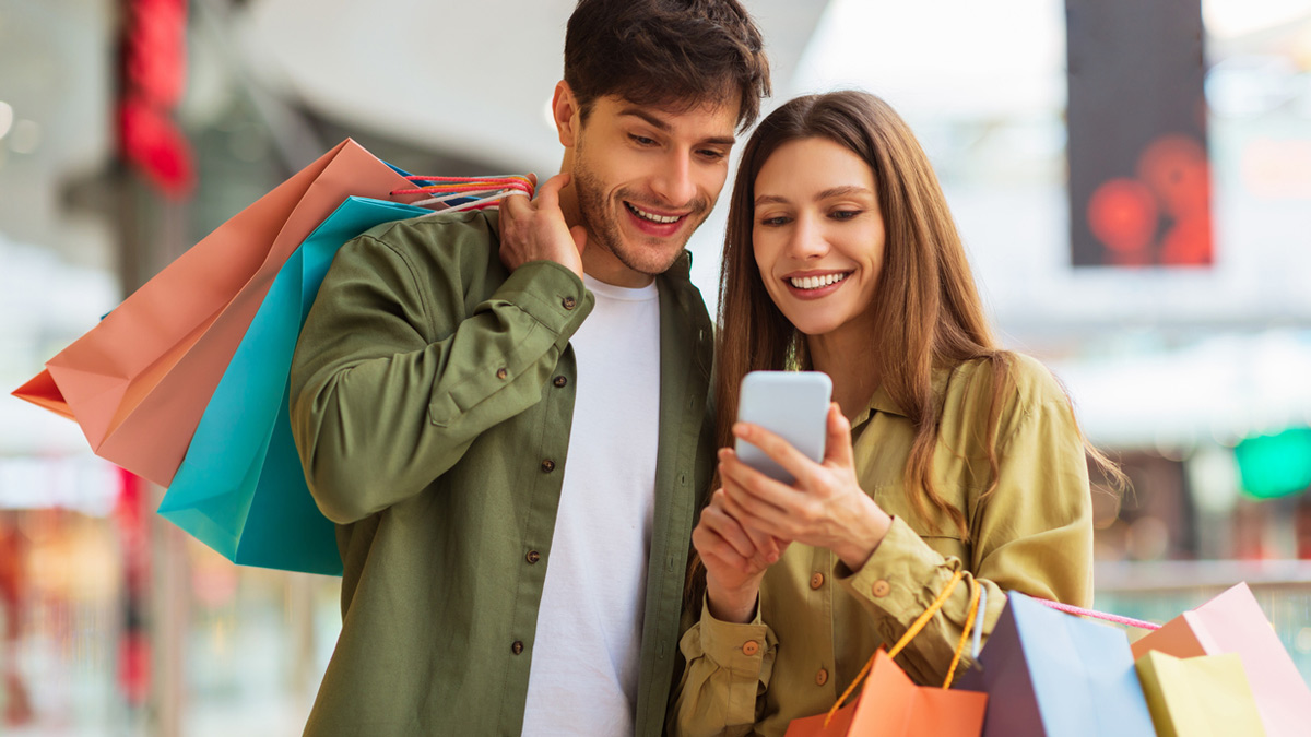 Man and woman with shopping bags looking at mobile phone and smiling