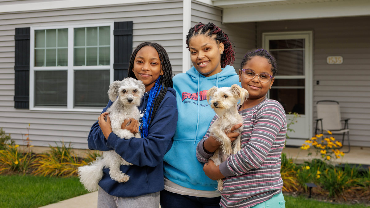 Woman and her two daughters, holding two dogs, in front of home.