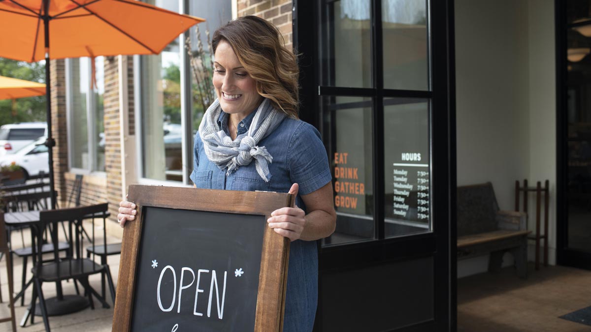 Woman placing open sign outside her retail store