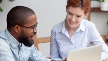 Two people talking to each other while looking at a laptop 