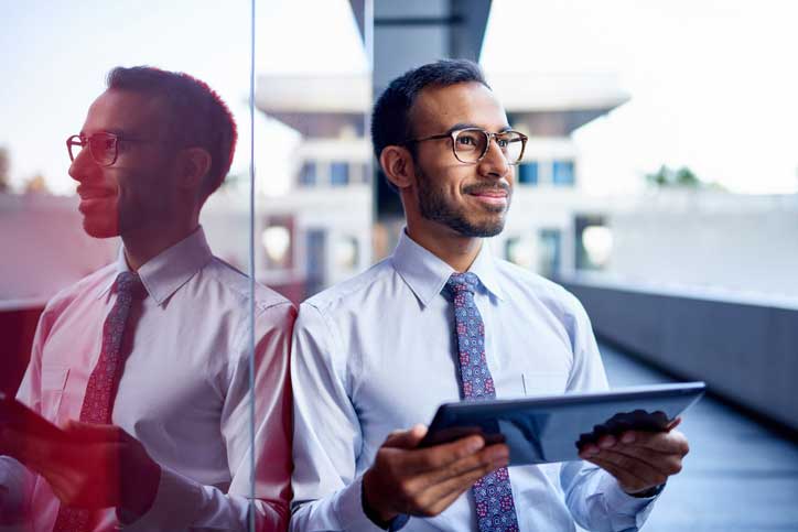 Young professional man standing against a glass wall while holding a tablet device