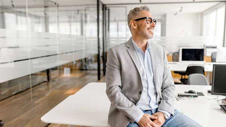 Man wearing a blazer casually sitting on a desk in a meeting room