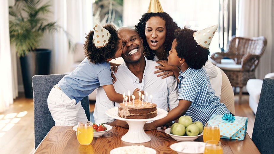 Una familia de raza negra con papá, mamá y dos hijos celebran el cumpleaños de papá con un pastel de cumpleaños con velas.